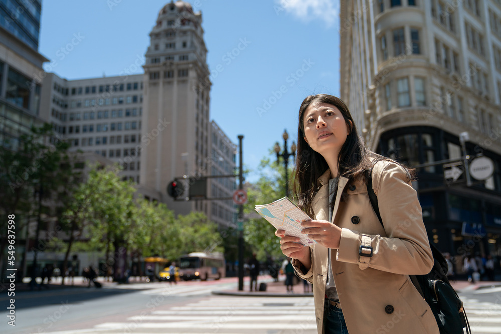 curious asian Japanese girl visitor looking around city with guide map while exploring downtown san Francisco in California usa near triangular office building on sunny day