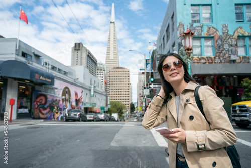 happy asian Korean girl traveler looking into distance enjoying streetscape with Transamerica Pyramid at background while visiting Chinatown in san Francisco California usa