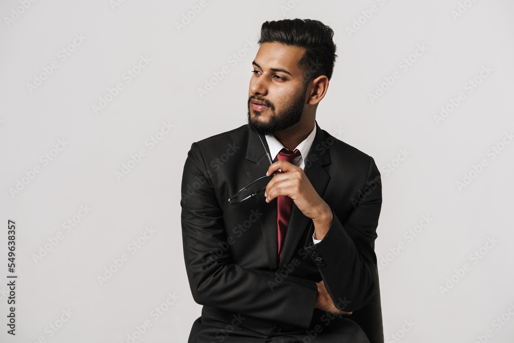 Young indian man wearing suit posing while sitting on chair Young indian man wearing suit posing while sitting on chair
