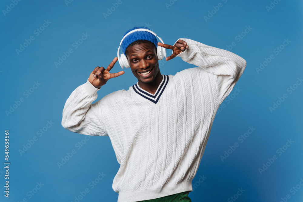 Naklejka premium Black young man gesturing and listening music with headphones