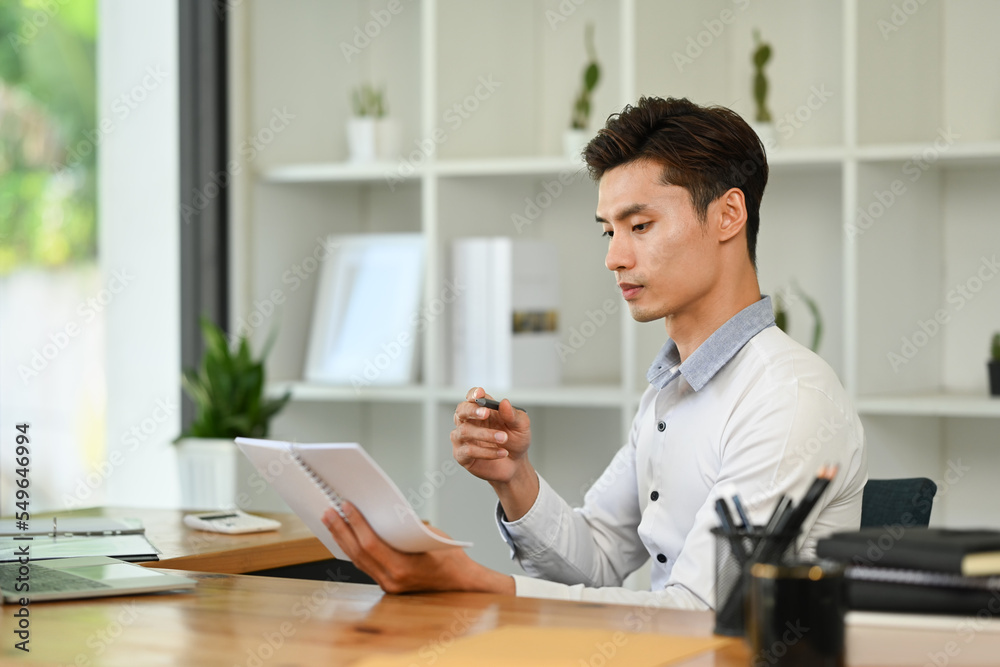 Side view of male manager analyzing weekly schedule in his notebook while sitting in modern workplace Side view of male manager analyzing weekly schedule in his notebook while sitting in modern workplace
