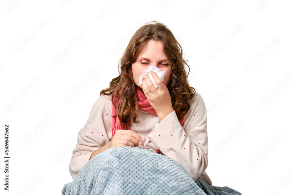 A sick woman blows her nose in a napkin, a runny nose, isolated on a white background. Adult ill woman with a red scarf sitting on a home bed in a white bedroom, female aged 35 years - obrazy, fototapety, plakaty 