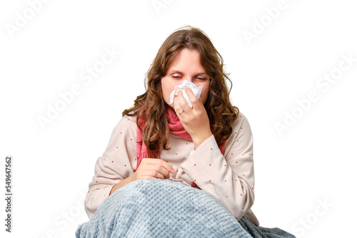 A sick woman blows her nose in a napkin, a runny nose, isolated on a white background. Adult ill woman with a red scarf sitting on a home bed in a white bedroom, female aged 35 years