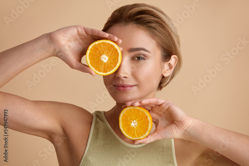 Beautiful Woman Smiling with Orange Fruit. Positive Woman with Radiant Face Recommended Vitamin for Skin. Girl Model with Natural Makeup and Glowing Hydrated Skin. Vitamin C Cosmetics Concept  photo