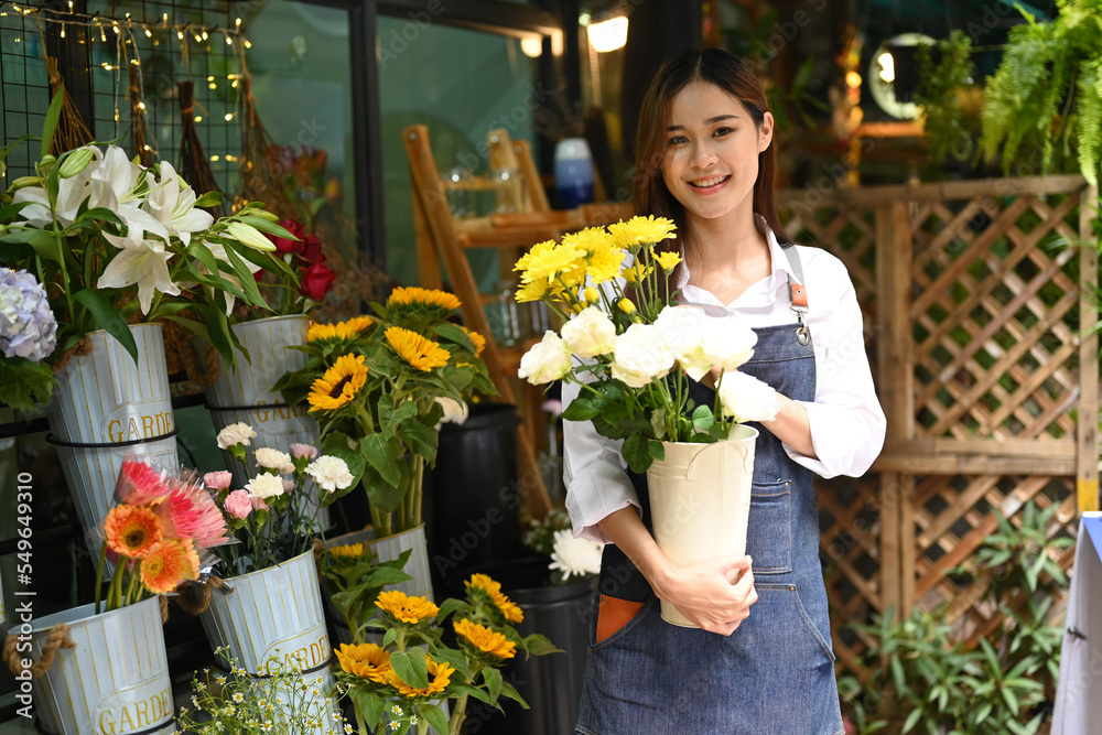 Portrait of gorgeous female florist holding beautiful bouquet while standing front of her flower shop