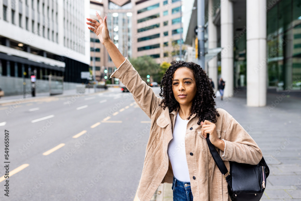 Woman standing on footpath hailing taxi in city