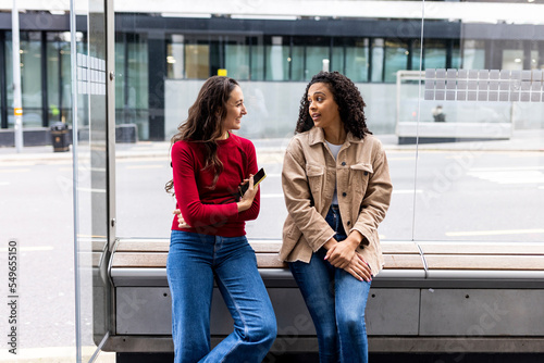Woman talking with friend sitting at bus stop photo