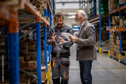 Young wearhouse worker walking accross wearhouse streets with his senior manager, discussing about problems in company and prepairing boxes for delivering © Nemanja