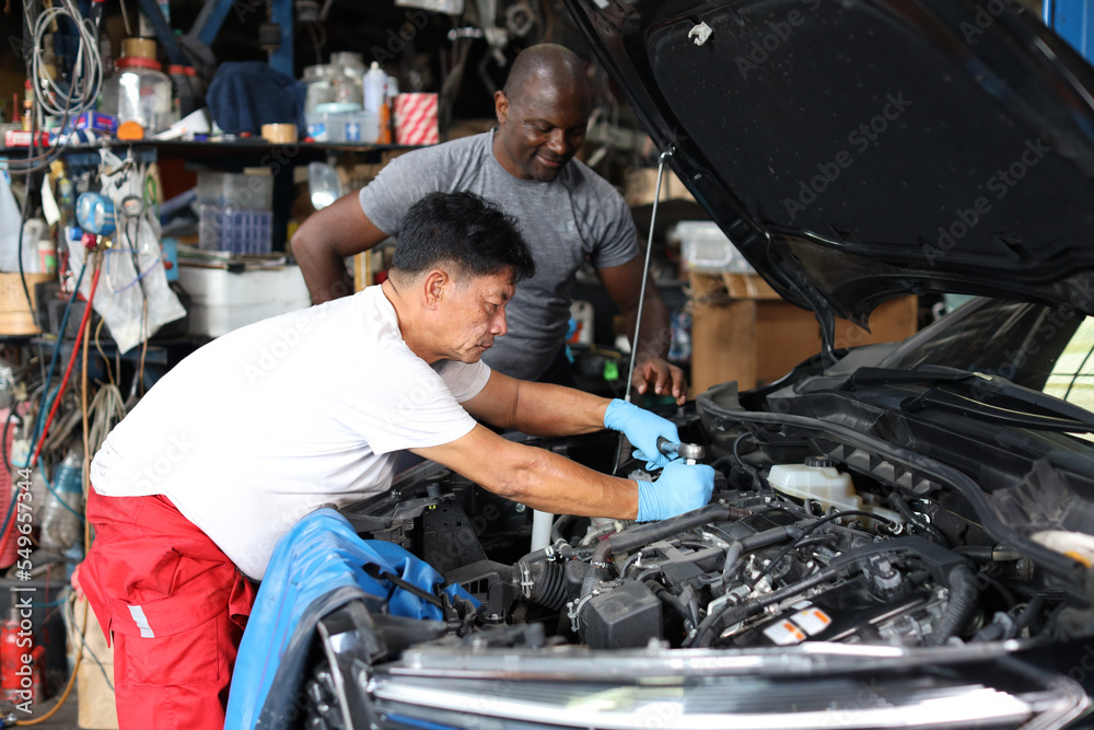 Group of car mechanic men in half uniform checking maintenance a car service at repair garage station. Worker holding wrench and fixing breakdown vehicle. Concept of car center repair service. Group of car mechanic men in half uniform checking maintenance a car service at repair garage station. Worker holding wrench and fixing breakdown vehicle. Concept of car center repair service.