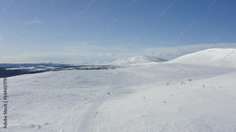 Aerial wide view of tourists riding snowmobiles through snow in northern Sweden during winter. Aerial wide view of tourists riding snowmobiles through snow in northern Sweden during winter.