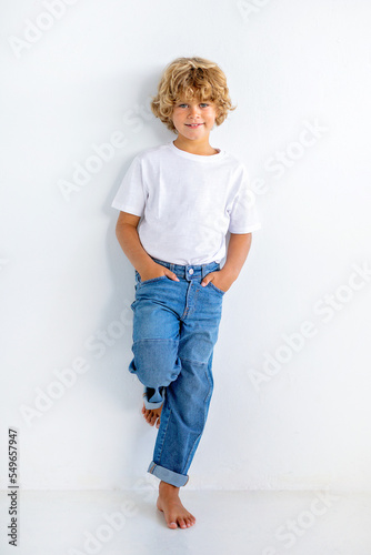 Cute boy with hands in pockets leaning on white background