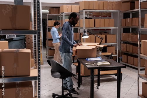 Storehouse manager preparing clients orders putting products in carton boxes, checking shipping details before delivery packages. Diverse team working in distribution center warehouse