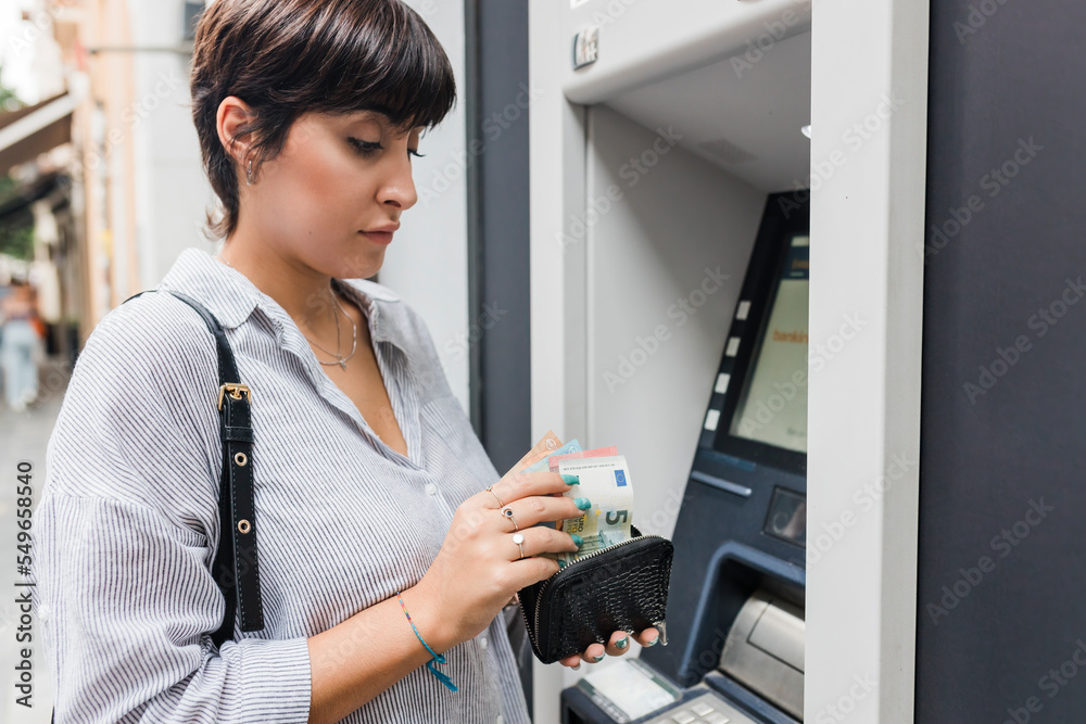 Young woman counting money from purse at ATM machine