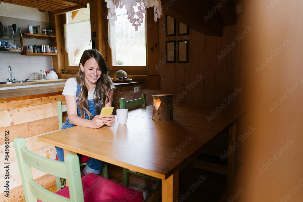 Smiling woman using smart phone at dining table in chalet Smiling woman using smart phone at dining table in chalet