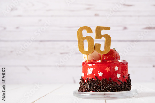 The number Sixty five on a red birthday cake on a light background