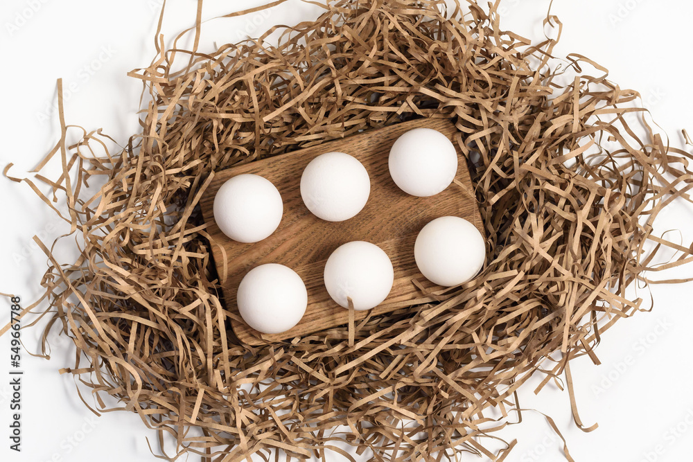 Chicken eggs on wooden rack and paper filling of stylized nest on white upper view. Organic farmer products for food cooking in light studio, top view, flatlay, Chicken eggs on wooden rack and paper filling of stylized nest on white upper view. Organic farmer products for food cooking in light studio, top view, flatlay,