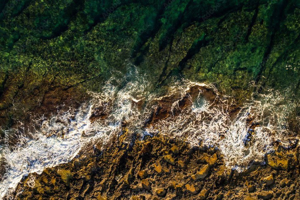 Ocean waves crashing on rocks on the beach, aerial drone view