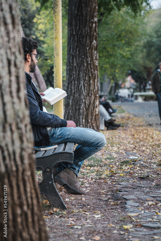 Fototapeta premium Man reading a book sitting on a bench in the park
