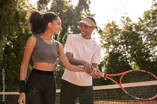 Young male coach teaching a curly-haired girl to play tennis