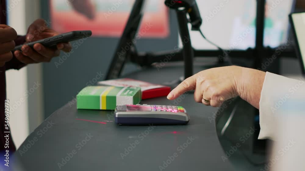 Male client buying vitamins with mobile phone nfc payment, using smartphone at pos terminal in drugstore. Person paying for medicaments and drugs at pharmacy counter. Close up. Handheld shot. Male client buying vitamins with mobile phone nfc payment, using smartphone at pos terminal in drugstore. Person paying for medicaments and drugs at pharmacy counter. Close up. Handheld shot.