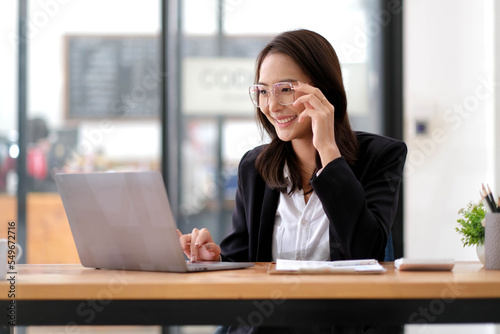 Portrait of happy business woman wearing glasses at workplace in office. Young handsome female worker using modern laptop