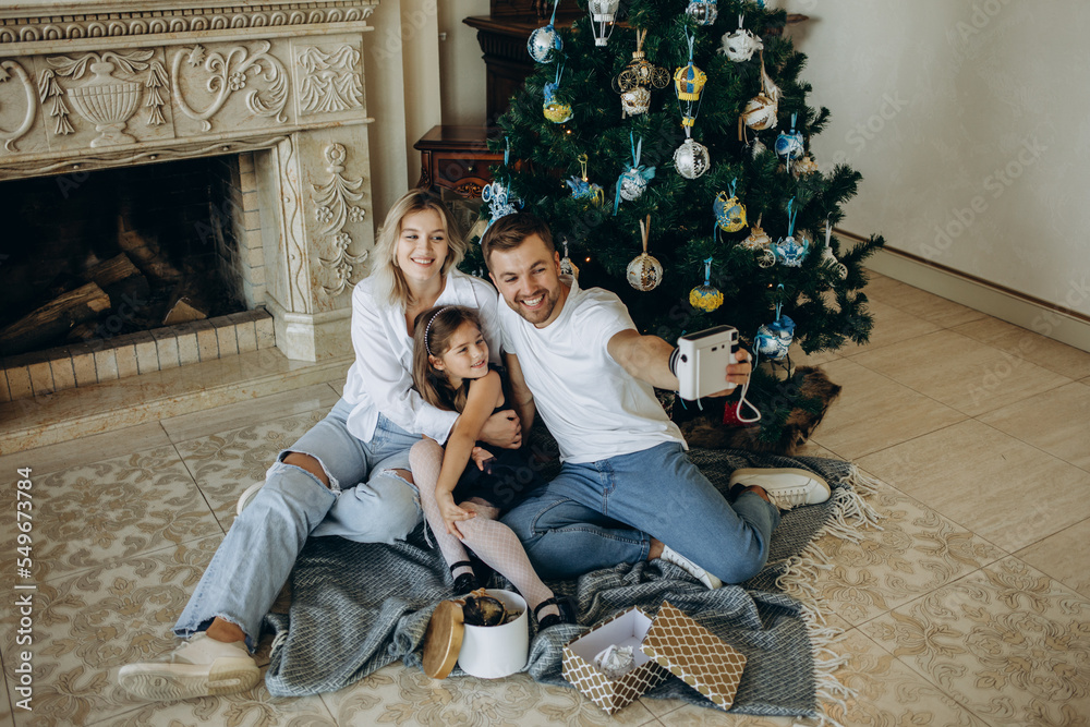 Merry Christmas and happy holidays. A young family takes a selfie against the background of a Christmas tree Merry Christmas and happy holidays. A young family takes a selfie against the background of a Christmas tree