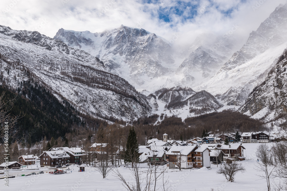 Traditional mountain village with snow. Macugnaga (Pecetto), Italy. Important ski resort in the European Alps with Monte Rosa partially shrouded in fog and clouds. Winter mountain landscape 
