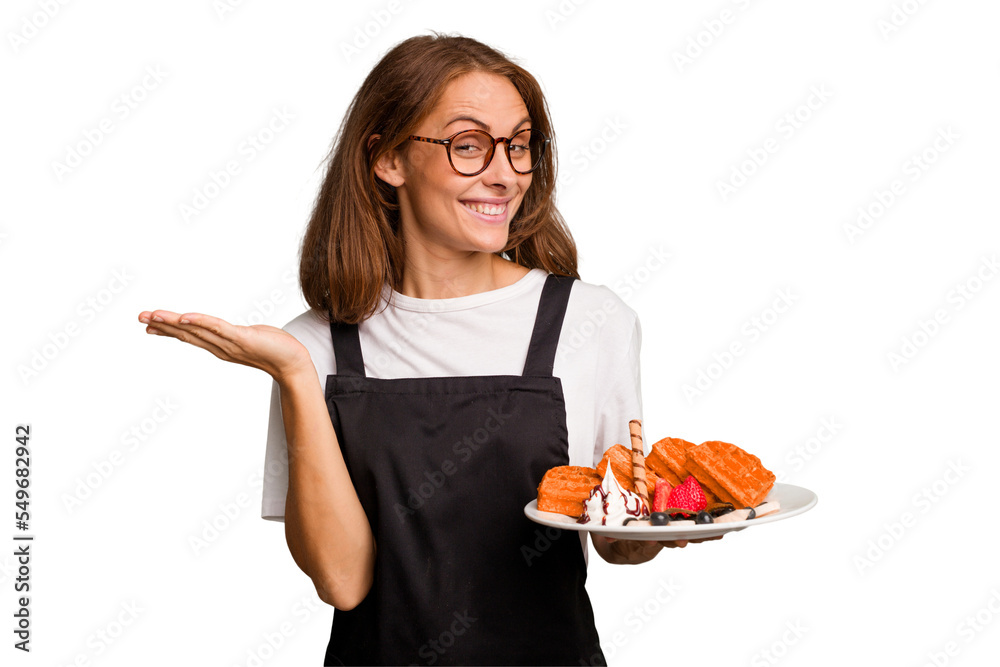 Young caucasian woman holding a waffles dish isolated showing a copy space on a palm and holding another hand on waist. Young caucasian woman holding a waffles dish isolated showing a copy space on a palm and holding another hand on waist.