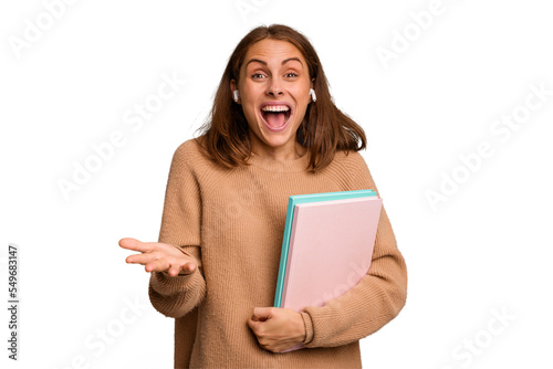 Young student woman holding a books isolated receiving a pleasant surprise, excited and raising hands.