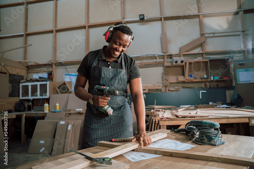 Hardworking black carpenter in factory with electric drill