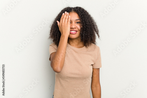 Young african american woman isolated on white background having fun covering half of face with palm.