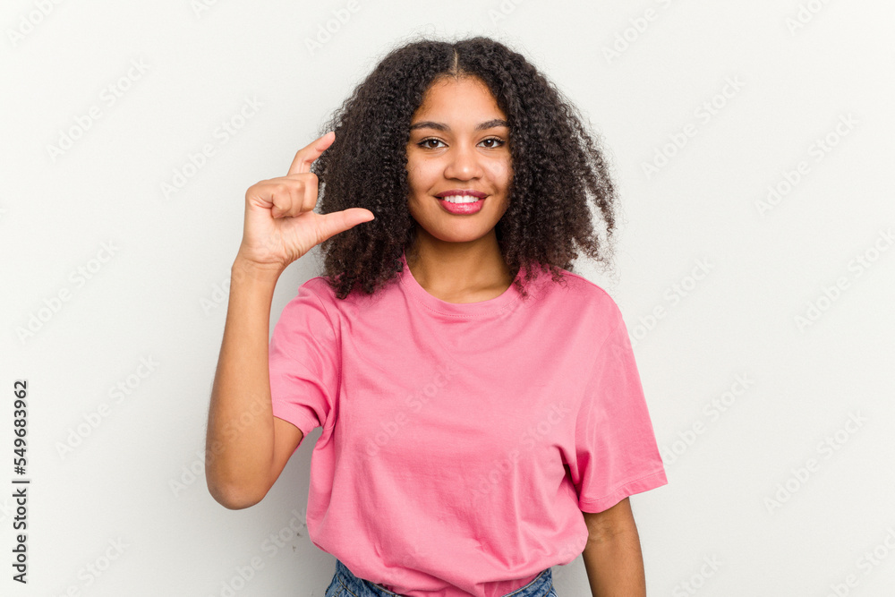 Young african american woman isolated on white background holding something little with forefingers, smiling and confident.