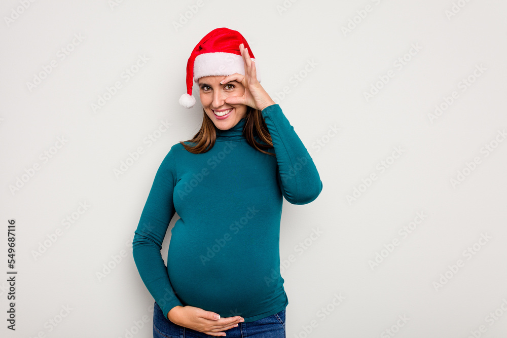 Pregnant caucasian woman wearing a christmas hat isolated on white background excited keeping ok gesture on eye. Pregnant caucasian woman wearing a christmas hat isolated on white background excited keeping ok gesture on eye.