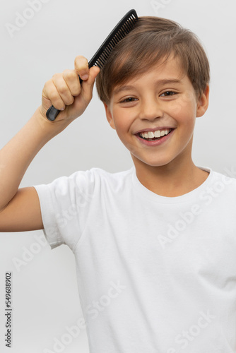 An young boy brushing his hair isolated on a white background.