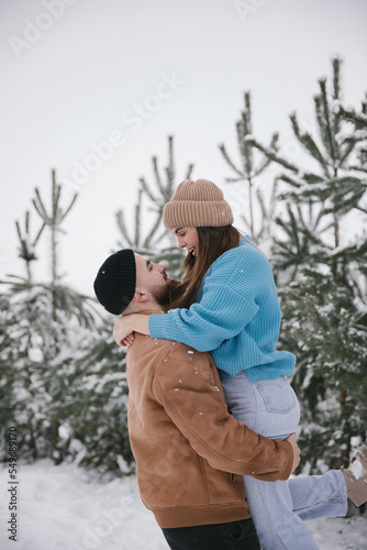 A man holds his beloved woman in his arms. Happy couple spend time in winter in snowy forest.