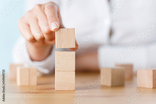 Businesswoman putting a new block on top of a block tower.