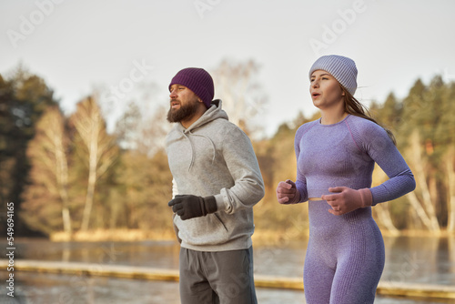 Adult caucasian couple running outdoors in the winter by the lake