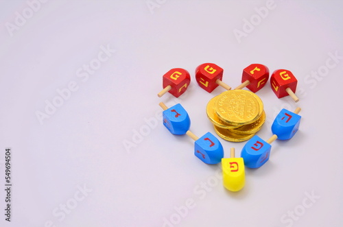Multicolor Heart dreidels and chocolate golden coins. Hanukkah and judaic holiday concept. Copy space on white background. Family game for the holiday of Light and love. Postcard and place for text