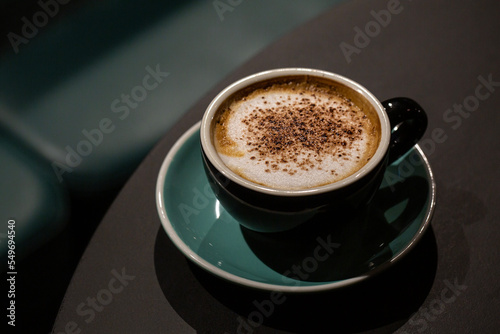 A cup of caffe cappuccino with cocoa chocolate powder. Coffee drink with steamed milk foam. Dark green background.