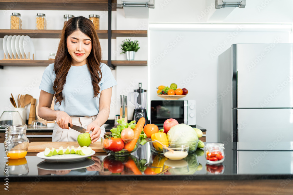 A happy young Asian woman preparing a healthy salad with fresh vegetables on a cutting board in the home kitchen. Food cooking for couple husband and wife in a good relationship. A happy young Asian woman preparing a healthy salad with fresh vegetables on a cutting board in the home kitchen. Food cooking for couple husband and wife in a good relationship.