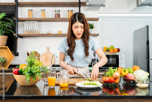 A happy young Asian woman preparing a healthy salad with fresh vegetables on a cutting board in the home kitchen. Food cooking for couple husband and wife in a good relationship.
