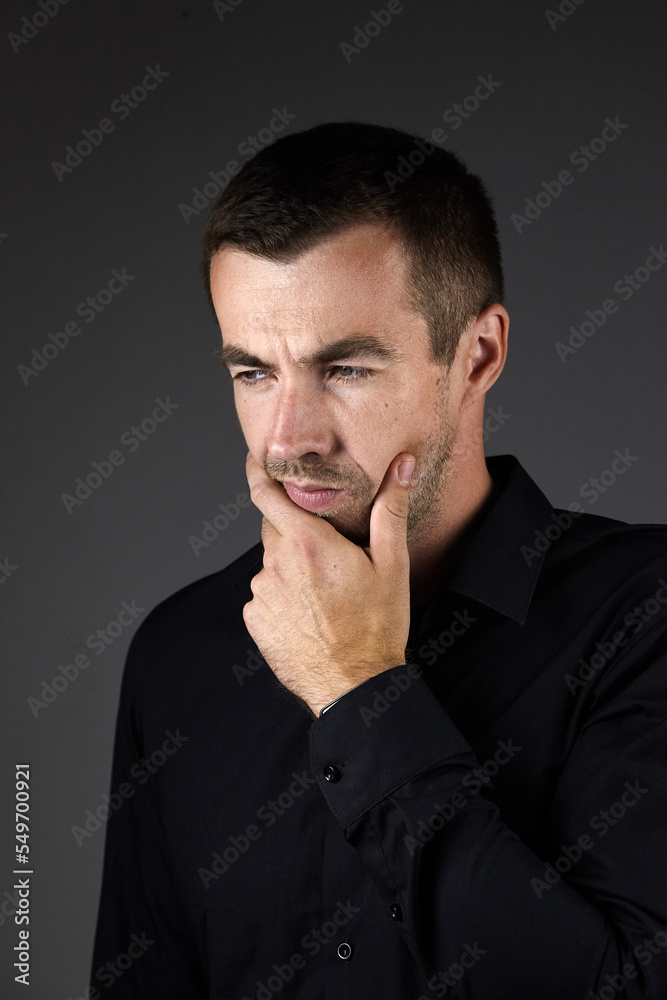 Portrait of pensive man in a black shirt on a dark background. Young caucasian dark-haired man