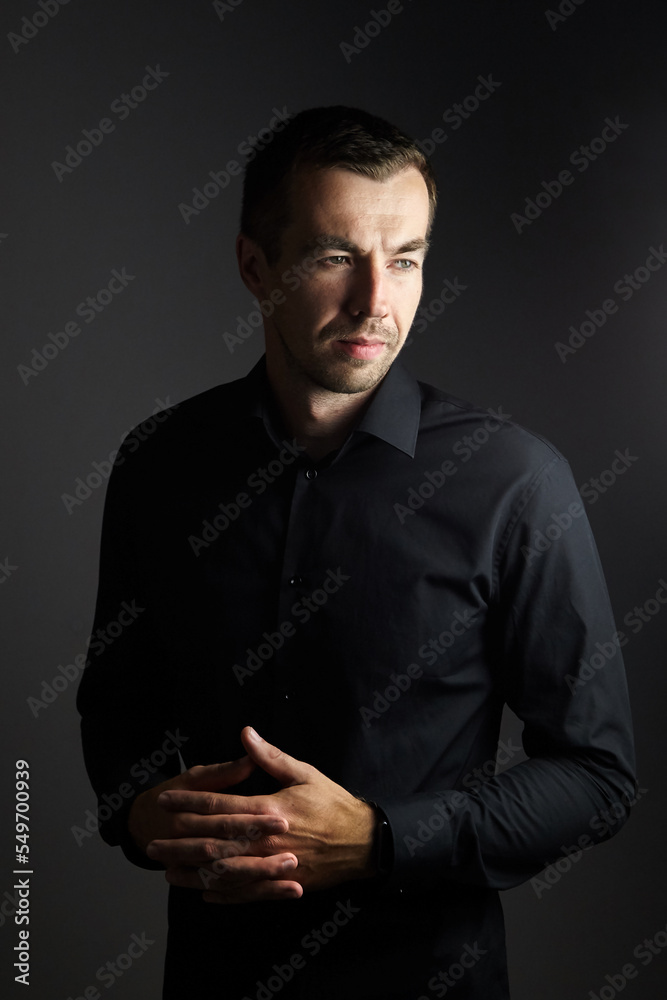 Portrait of man in a black shirt on a dark background. Serious brunet with arms folded. Young caucasian man