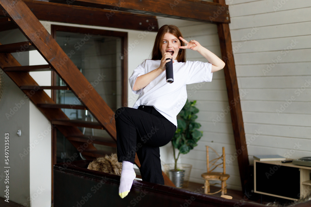 Positive attractive woman dances and sings into a fictional microphone at home in a modern interior. Positive attractive woman dances and sings into a fictional microphone at home in a modern interior.