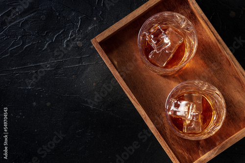 Whiskey in glasses with ice. Bourbon whisky on rocks on a black slate background, overhead flat lay shot with copy space