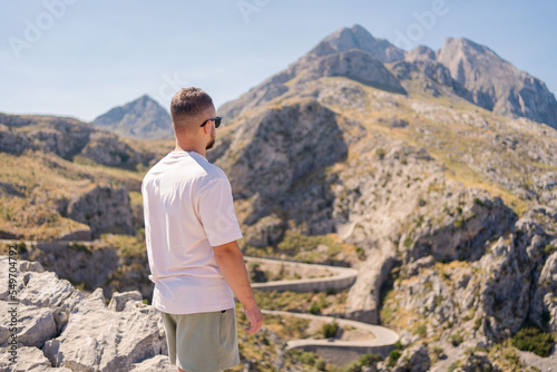 A man stands on a top of the mountain looking at beautiful summer mountain landscape on hiking trip