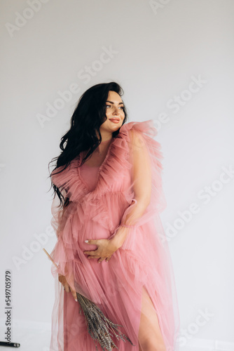 Beautiful pregnant woman in elegant dress posing to photographer in studio