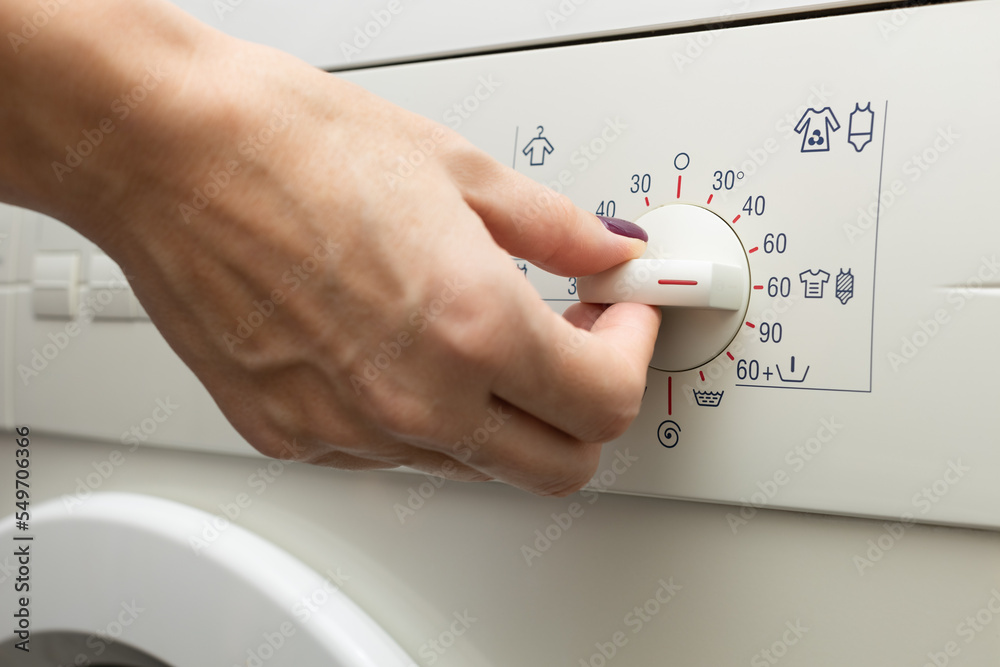a man chooses a mode on a washing machine - obrazy, fototapety, plakaty 