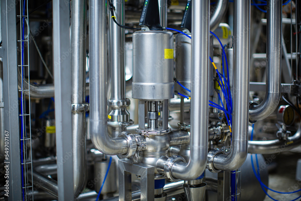The process pipe valve is stainless at the in-process area of the pipeline flowing stainless food milk in a factory at the control room The process pipe valve is stainless at the in-process area of the pipeline flowing stainless food milk in a factory at the control room