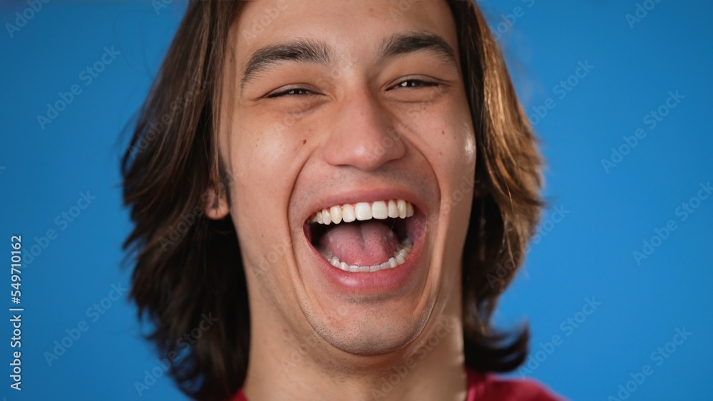 Closeup portrait of smiling handsome Hispanic Latino gender fluid young man 20s wearing red casual shirt isolated on blue color background in studio. Sincere emotions lifestyle concept Closeup portrait of smiling handsome Hispanic Latino gender fluid young man 20s wearing red casual shirt isolated on blue color background in studio. Sincere emotions lifestyle concept
